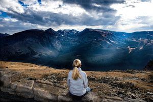 Eduquer Avec Sagesse - Photo by Donald Giannatti on Unsplash - jeune femme blonde en bleu de dos devant un paysage de montagne et ciel et nuages bleus en train de contempler