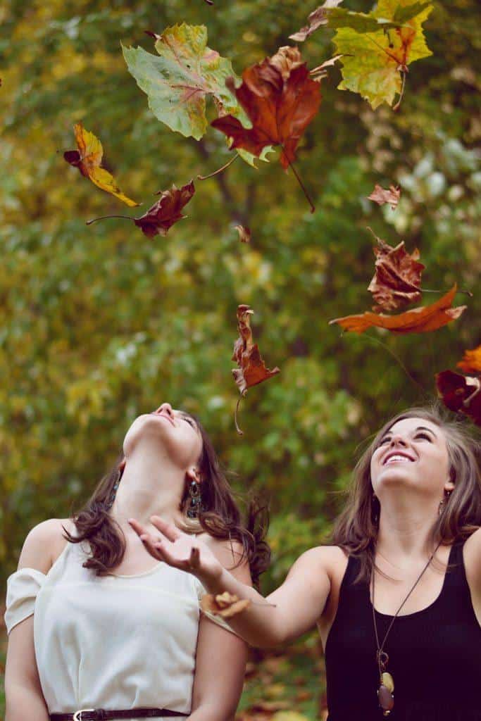 Eduquer avec sagesse - photo de evelyn-sur-unsplash-deux jeunes filles dans la nature jetant des feuilles d'automne en regardant vers le ciel