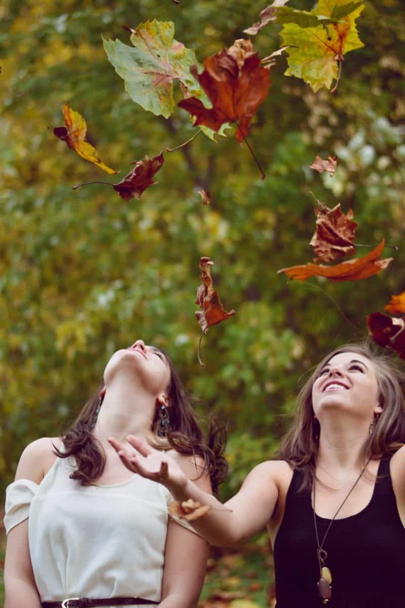 Eduquer avec sagesse - photo de evelyn-sur-unsplash-deux jeunes filles dans la nature jetant des feuilles d'automne en regardant vers le ciel
